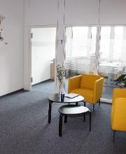 Das Bild zeigt den Eingangsbereich. Hier sieht man zwei gelbe Sessel und einen Tisch sowie einen Garderobenständer und eine kunstvolle Weltkarte an der Wand.