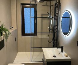 Modernes Bad mit Walk-in-Dusche: Barrierefreie Dusche mit schwarzem Rahmen, beleuchtetem Rundspiegel und fugenlosen, eleganten, grauen Wandflächen.