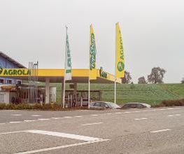 AGROLA Tankstelle in Ettiswil mit TopShop. Strasse im Vordergrund . Mittig drei grosse Fahnen - Landi, TopShop und AGROLA Fahnen. Dahinter AGROLA und TopShop.
