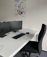 Arbeitsplatz mit zwei Bildschirmen, Tastatur, Maus und Headset sowie einem schwarzen Bürostuhl.