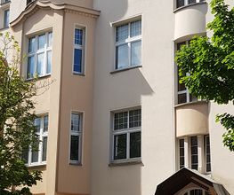 Gelbes Gebäude mit Vorsprung und Überdachter Eingangstür. Davor parkt ein Auto.
