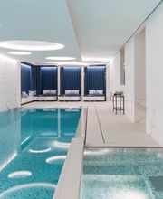 Indoor swimming pool with sleek modern design, white marble walls, and lounge chairs at The Woodward Geneva.