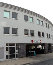 Außenansicht des Gebäudes, Halbrunde Form und helle Fassade. Im Erdgeschoss befindet sich ein Parkhaus.