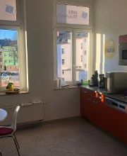 Rote Küche mit Spülmaschine, Kaffeemaschine, Wasserkocher und Mikrowelle. Daneben ein Tisch mit mehreren Stühlen.