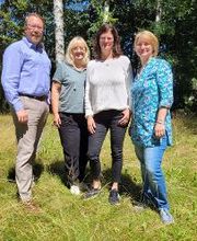 Ein Gruppenbild vom Standortteam. 4 Personen stehen an einem sonnigen Tag draußen im Grünen.