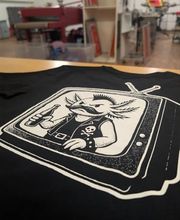 Detailreicher Motiv-Druck im klassischen Siebdruckverfahren auf schwarzem Baumwoll-Shirt. In unserer Leipziger Manufaktur realisieren wir feine Linienführungen, scharfe Kontraste und deckende Farbaufträge. Dieser Druck eignet sich perfekt für kreatives Band-Merchandise, Illustrationen von Künstlern und hochwertige Streetwear-Kollektionen. Als Experten für Textildruck in Leipzig beraten wir euch zur optimalen Umsetzung eurer Artworks.