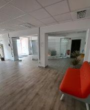 Eingangsbereich mit Säule. Links ein Arbeitsplatz und eine Pflanze, rechts ein rotes Sofa und Pflanzen. 