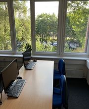 2 Arbeitsplätze vor einer Fensterfront mit Blick ins Grüne. Auf den Tischen befinden sich 2 Computerbildschirme mit dazugehöriger Tastatur und Maus.