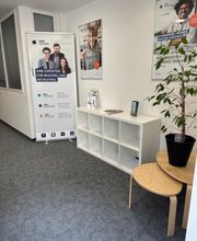 Ein Regal mit Flyern, daneben ein Roll Up Banner und eine Pflanze auf Beistelltischen. Über dem Regal hängen 2 Plakate der WBS TRAINING.