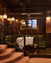 An intimate corner table with green velvet seating, white tablecloth, and warm wall sconces, positioned beside a carpeted staircase with decorative ironwork.
