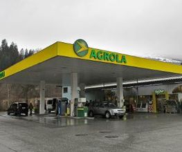 AGROLA Tankstelle in Thusis mit TopShop. Grosse Überdachung. Autos am Tanken. Regnerische Aufnahme. Grosser Vorplatz.