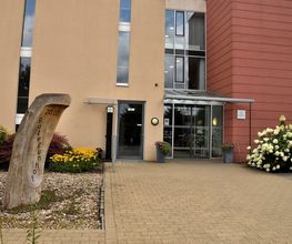 Haus Botegunhof Achim – Eingang mit Holzskulptur „2010 Botegunhof" und sommerlicher Begrünung