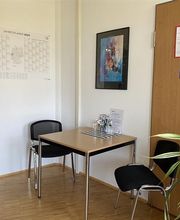 Beratungsecke mit einem Tisch und 2 Stühlen. An den Wänden hängen ein Kalender sowie ein Bild. Rechts steht eine grüne Zimmerpflanze.