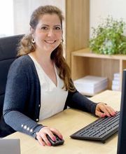 Portrait von Rasha Zeidan, Bildungsreferentin am WBS Standort Güstrow. Sie hat dunkelblonde Haare und sitzt vor ihrem Computer und lacht freundlich in die Kamera.