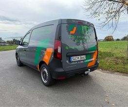 Kompakter Firmen-Transporter mit auffälliger Teilfolierung in Grün, Orange und Schwarz. Das dynamische Design verbindet Markenfarben, Logo und Kontaktdaten zu einer aufmerksamkeitsstarken Fahrzeugbeschriftung.