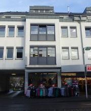 ein vierstöckiges, weißes Gebäude mit Ladenzeile im Erdgeschoss.