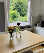 Küche mit Tisch und Stühlen. Auf dem Tisch steht eine kleine Blumenvase und eine Wasserflasche.