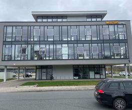 mediaService Bremen | Full-Stack Werbeagentur - Die Außenansicht eines modernen, dreistöckigen Bürogebäudes mit einer großen Glasfassade und davor geparkten Fahrzeugen an einer Straße.