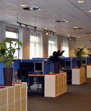 Trainingsraum mit Fachablagen vor den Schreibtischen mit je zwei PC-Bildschirmen. Auf den schränken stehen schöne, grüne Zimmerpflanzen.