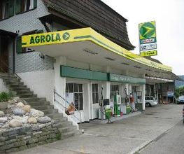 AGROLA Tankstelle in Rüegsbach, bei Autogarage; leicht gebogenes Dach mit Logo-Schild angebracht, zwei Tanksäulen, rechts Autogarage, links Treppe zu Wohnhaus