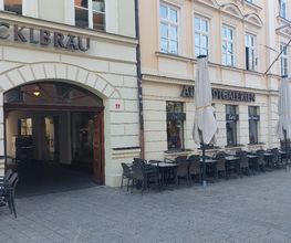 Fassade eines Gebäudes mit Torbogen zum Eingang. Angrenzend ein Café mit Außensitzplätzen.
