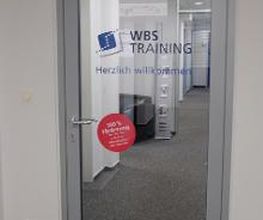 Eine Glastür mit der Aufschrift "WBS TRAINING" und "Herzlich Willkommen".