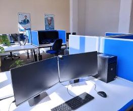 Arbeitsbereich mit 2 Computer-Bildschirmen, einer Tastatur, Maus und blauen Trennwänden. Der Raum ist hell und geräumig.