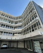 Außenansicht vom Gebäude mit heller Fensterfassade und Parkmöglichkeiten.