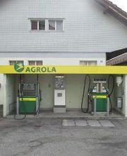 AGROLA Tankstelle in Menzingen. Zwei Tanksäulen mit Zahlterminal unter kleinem Vorstand. Im Hintergrund Gebäude mit grauer Fassade.