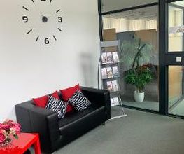 Aufenthaltsraum mit einem schwarzen Ledersofa, roten Kissen und einem roten Beistelltisch. Darüber hängt eine stilvolle, große Uhr an der Wand.