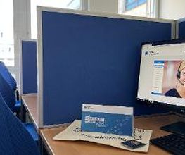 Arbeitsplatz bestehend aus 2 PC-Bildschirmen, Tastatur, Maus sowie einem blauen Bürostuhl und blauen Trennwänden.