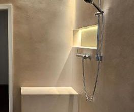 Sitzbank in der Dusche: Komfortable, geflieste Sitzgelegenheit in einer modernen, fugenlosen Dusche mit warmer Wandfarbe und dunkler Armatur.