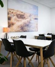 Aufenthaltsraum mit Tischen und Stühlen. Ein großes Bild von einem Strand hängt an der Wand.