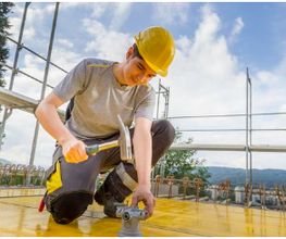 Montage-Elektiker Lehrling der mit Hammer und Helm ausgerüstet auf der Baustelle bei der Arbeit ist.