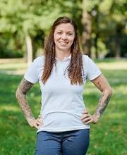 Vanessa Tonn steht im weißen T-Shirt mit WBS GRUPPE Logo in der grünen Natur und lächelt freundlich.