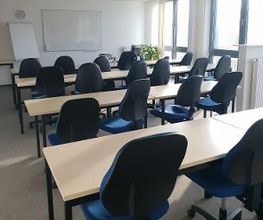 Schulungsraum für Präsenzkurse, viele Tische in einer Reihe mit Stühlen