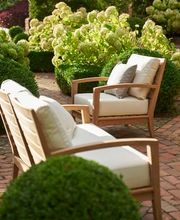 Zwei elegante Gartenstühle mit hellen Polstern stehen einladend inmitten eines gepflegten Gartens mit üppig blühenden Hortensien. Die harmonische Komposition strahlt Ruhe, Komfort und natürliche Schönheit aus.