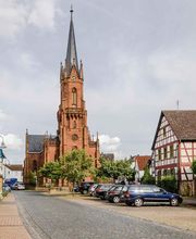Der älteste Nachweis über ein Gotteshaus in Langstadt stammt aus dem Jahre 1482: Erwähnt wird eine Kapelle, die in der Ortsmitte stand. 1523 wird die Kapelle erweitert, 1561 wird Langstadt selbstständige Pfarrei. Im 18. Jahrhundert folgen weitere Erweiterungen. 1877 wird das Kirchengebäude abgebrochen, weil es zu klein geworden war. An dessen Stelle entsteht von 1878 bis 1880 der große neugotische Bau der heutigen Pfarrkirche.