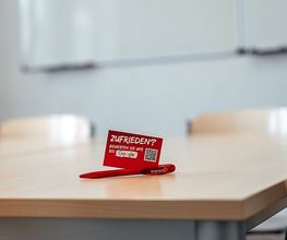 Beispiel Unterrichtsraum vor Ort mit Tisch, Stühlen und White Board an der Wand.