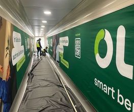 mediaService Bremen | Full-Stack Werbeagentur - Zwei Werbetechniker bei der Montage einer großflächigen grünen Wandverkleidung mit Werbeaufdrucken und QR-Code in einem langen Korridor.