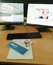 PC-Arbeitsplatz mit mehreren Monitoren, Tastatur und Maus. Davor liegen Schulungsunterlagen.