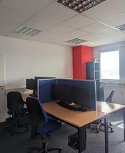 Schulungsraum mit mehreren Arbeitsbereichen, die durch blaue Trennwände voneinander abgegrenzt sind und mit PC-Bildschirmen, Tastatur, Maus und Headset ausgestattet sind. Blaue Bürostühle.