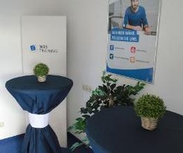 Beratungsbereich mit mehreren Bistrotischen, die mit blauen Hussen überzogen sind. Darauf stehen Tischpflanzen.