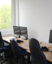 Arbeitsbereich ausgestattet mit 2 Bildschirmen, einer Tastatur, Maus und Headset. Fenster mit Blick ins Grüne.
