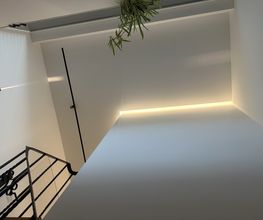 Individuelle Treppenhausgestaltung mit Q4-Oberflächen, indirekter LED-Beleuchtung und flächenbündig integrierten 48-V-Magnetschienen.