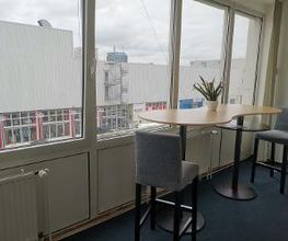 Sitzgelegenheit am Fenster bestehend aus einem modernen Hochtisch und 2 Stühlen. Auf dem Tisch steht eine Topfpflanze.