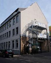 Außenansicht des Gebäudes, in dem sich die Räumlichkeiten der WBS Training befinden. Graue Fassade, Wendeltreppe an der Fassade mit Werbebanner von „WBS TRAINING“.