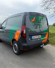 Kompakter Firmen-Transporter mit auffälliger Teilfolierung in Grün, Orange und Schwarz. Das dynamische Design verbindet Markenfarben, Logo und Kontaktdaten zu einer aufmerksamkeitsstarken Fahrzeugbeschriftung.