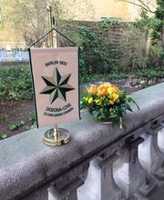 Ein kleiner Wimpel der Dodona Loge Berlin neben einem Blumengesteck.