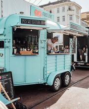 FirstLoveCoffee GmbH - Kaffee Catering Berlin - Mobile Kaffeebar mit Branding, Sonnenschirmen, Liegestühlen und Barista bei urbanem Event, ideal für Kaffee Catering mit frischen Waffeln.